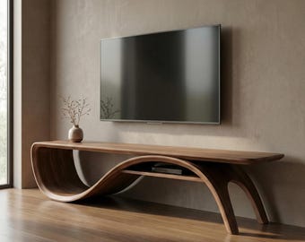 May include: A long, curved wooden media console with a smooth, continuous wave-like frame and a lower shelf. A flat-screen television is mounted on the wall above the console, and a small ceramic vase with dried branches sits on the left side.
