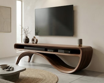 May include: A dark wood media console with a curved, continuous base and an open shelf holding electronic devices. A flat-screen television is mounted on the wall above the console, which is decorated with a vase and a small speaker.