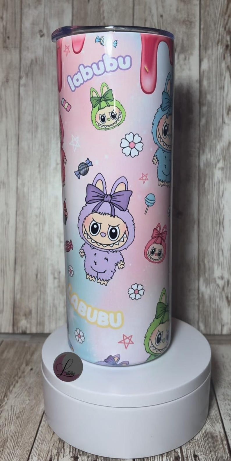 Op de afbeelding: Een cilindrische beker met een kleurrijk ontwerp met cartoonfiguren, snoepjes en het woord "labubu". De beker heeft een roze, blauwe en paarse gradi&euml;nt achtergrond met een roze deksel en een witte basis.