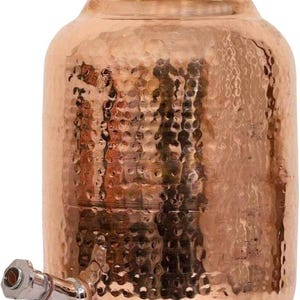 May include: A copper water dispenser with a hammered texture. The dispenser has a rounded body, a lid with a gold-coloured knob, and a silver-coloured spigot. The overall design is traditional and decorative.