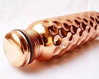 May include: A copper water bottle with a hammered texture. The bottle has a rounded shape with a screw-on cap. The copper has a shiny, metallic finish. The bottle is designed for carrying water.
