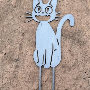 May include: A metal cat garden stake with a smiling face, whiskers, and a curved tail. The cat is silver and has two stakes at the bottom for easy placement in the garden. The cat is sitting and has a happy expression.