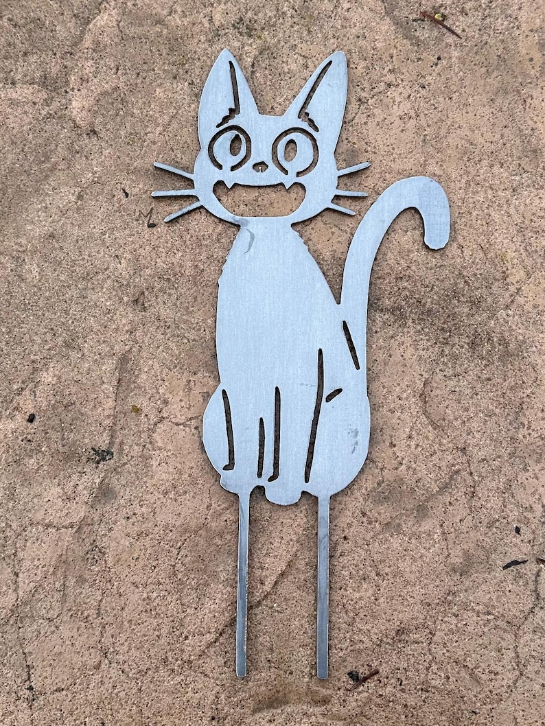 May include: A metal cat garden stake with a smiling face, whiskers, and a curved tail. The cat is silver and has two stakes at the bottom for easy placement in the garden. The cat is sitting and has a happy expression.