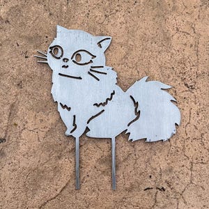 May include: A metal cat garden stake. The cat is depicted in a stylized, cut-out design with whiskers and a fluffy tail. The stake has two prongs for easy placement in the garden.