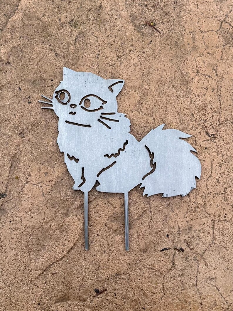 May include: A metal cat garden stake. The cat is depicted in a stylized, cut-out design with whiskers and a fluffy tail. The stake has two prongs for easy placement in the garden.