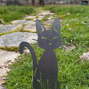 May include: A dark gray metal cat silhouette garden art piece. The cat is sitting upright with its tail curved. The cat is placed in a grassy area with a stone path and a gazebo in the background.