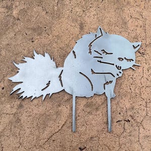 May include: A metal cat silhouette garden stake. The cat is depicted in a sitting position with a fluffy tail and pointed ears. The metal has a silver color and is designed to be placed in the ground.