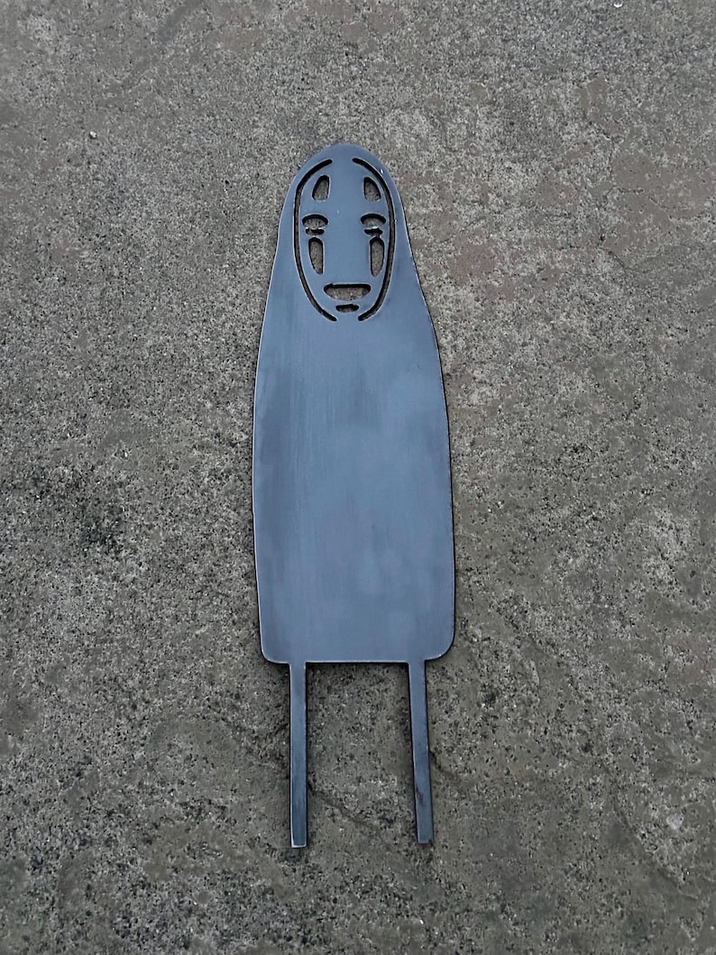 May include: A gray metal cutout of the character No-Face from the animated film Spirited Away. The cutout features the character's distinctive mask-like face and long, flowing body with two legs extending from the bottom.