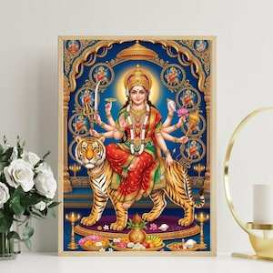 May include: A framed print depicting a multi-armed deity riding a tiger. The deity wears a crown and red and green garments. The background is blue with ornate gold detailing. The tiger is orange and black.
