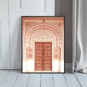 May include: Framed print of an ornate, carved wooden door with an arched entryway. The door is a reddish-brown color, and the archway features intricate patterns in shades of red and white. The print is set against a neutral background.