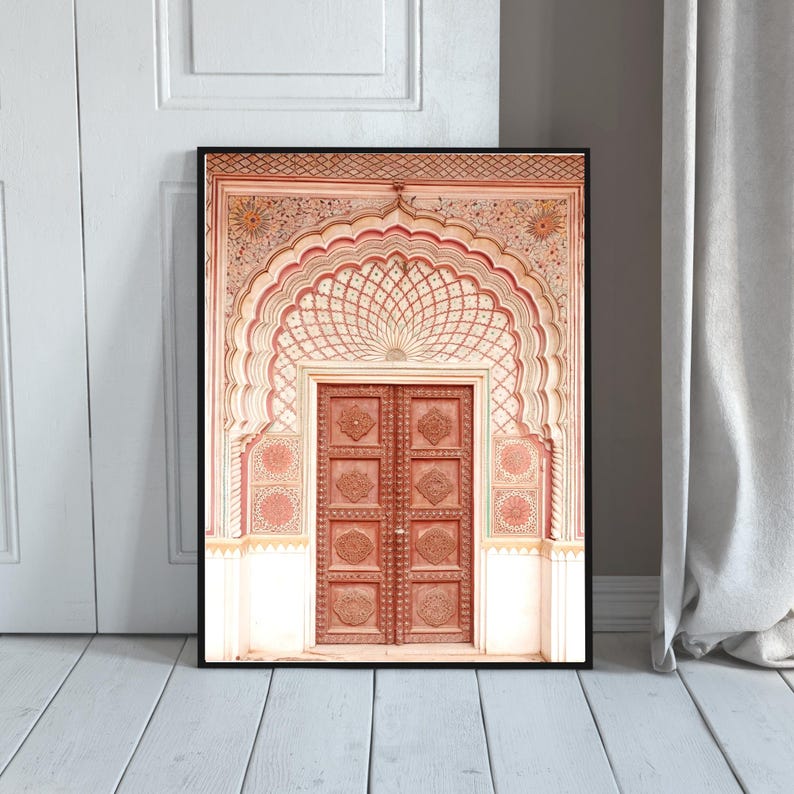 May include: Framed print of an ornate, carved wooden door with an arched entryway. The door is a reddish-brown color, and the archway features intricate patterns in shades of red and white. The print is set against a neutral background.