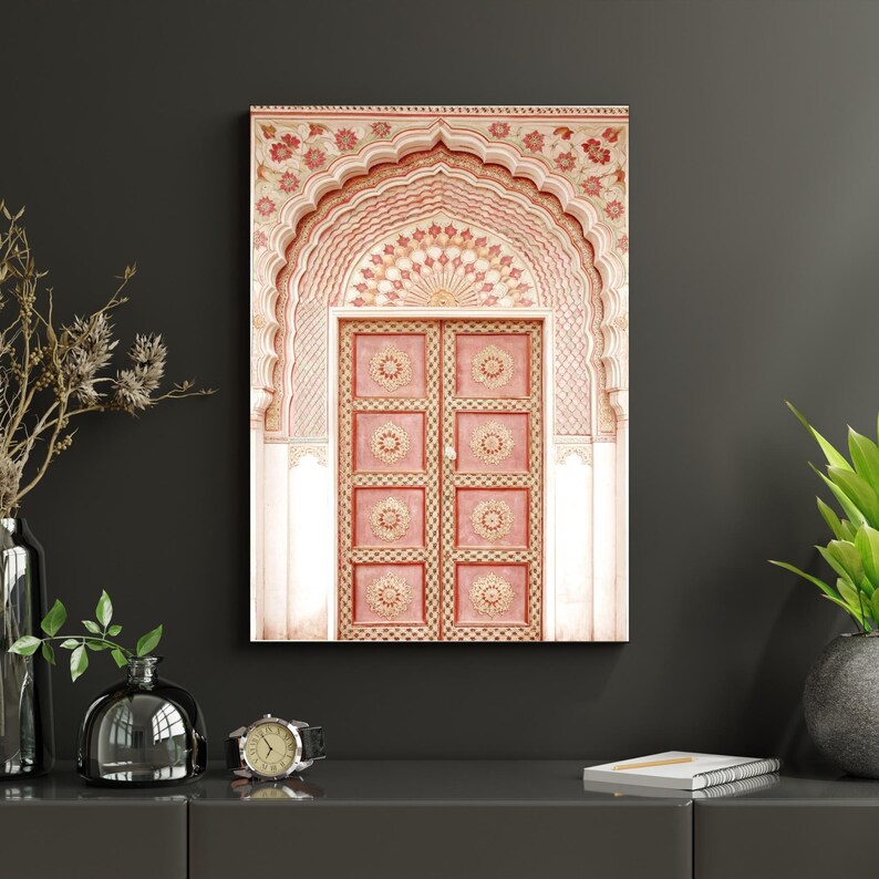 May include: A framed print of an ornate, pink door with a detailed archway. The door is divided into eight panels, each with a circular design. The archway and door frame feature intricate floral patterns in shades of pink and gold.
