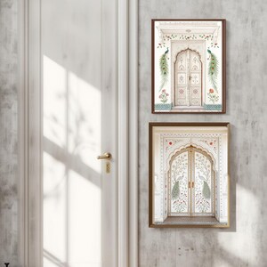 May include: Two framed art prints featuring ornate white doors with floral and peacock designs. The prints have brown frames and are set against a textured gray wall. The door designs include red and green floral accents.