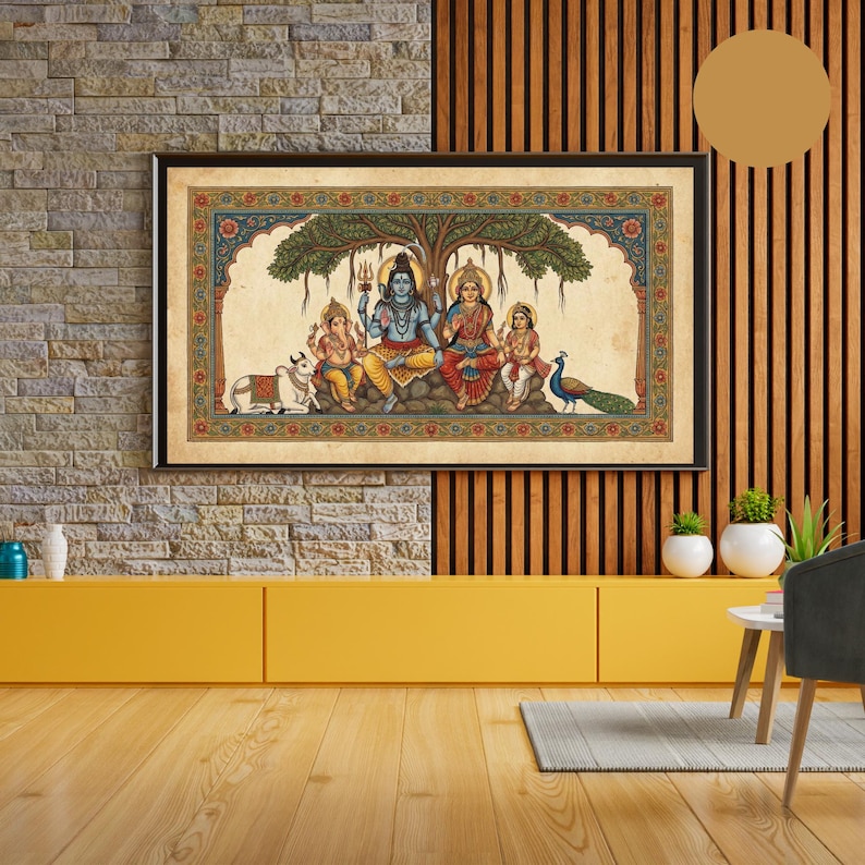 Puede incluir: Un retrato familiar hind&uacute; colorido y enmarcado. La obra representa una deidad central con piel azul, sentada con una mujer y dos ni&ntilde;os bajo un &aacute;rbol. Una vaca, un pavo real y un borde adornado completan la escena. El marco es negro.