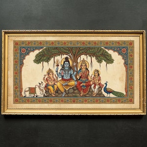 May include: A framed, colorful painting depicting a Hindu family under a tree. The artwork features figures in traditional attire, with a peacock and a cow. The frame is gold-colored, and the painting has intricate details and vibrant colors.