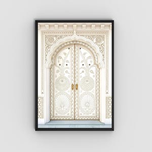 May include: A framed print featuring a detailed, ornate white door with gold accents. The door has an arched top and is decorated with intricate floral and geometric patterns. The frame is black, and the overall aesthetic is elegant and artistic.