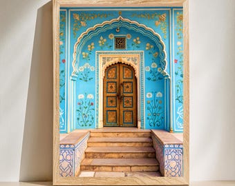 May include: A framed print of a vibrant blue wall with an arched doorway and ornate floral designs. The wooden door is golden, and steps lead up to it. The frame is made of light-colored wood, and the overall aesthetic is reminiscent of Indian architecture.