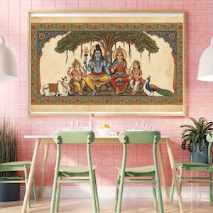 Puede incluir: Una obra de arte hind&uacute; enmarcada y colorida que representa a una familia bajo un &aacute;rbol. Las figuras centrales est&aacute;n sentadas, con una vaca, un pavo real y otras figuras. La obra de arte est&aacute; en un marco de madera y cuelga de una pared de azulejos rosas.