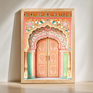 May include: A framed print depicting a traditional Indian door. The artwork features a pink door with detailed floral and tree designs, framed by an archway and columns in shades of pink, green, and orange. The frame is made of light-coloured wood.