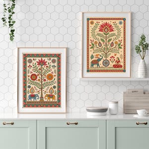 May include: Two framed art prints with a beige background and colorful floral and elephant designs. The prints have a gold frame and are displayed on a white countertop. The art features a tree with a large flower at the top and elephants at the base.
