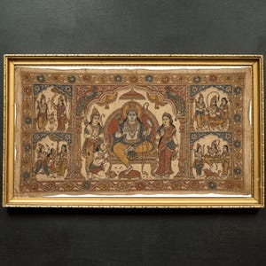 Op de afbeelding: Een ingelijst, kleurrijk Indiaas kunstwerk dat een centrale figuur op een troon afbeeldt, omringd door andere figuren in traditionele kledij. Het kunstwerk heeft ingewikkelde details en een goudkleurige lijst.