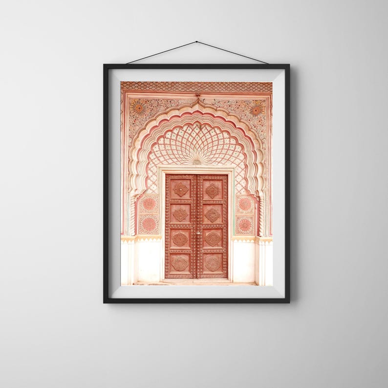 May include: Framed print of an ornate, arched doorway with a carved wooden door. The doorway features intricate patterns in shades of red, cream, and brown. The artwork is displayed in a black frame, hanging against a white wall.
