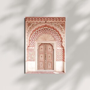 May include: A framed print of an ornate, arched doorway. The door and archway are painted in shades of red, pink, and cream, with intricate floral and geometric patterns. The door is centered within the arch, and the overall design evokes a sense of traditional architecture.