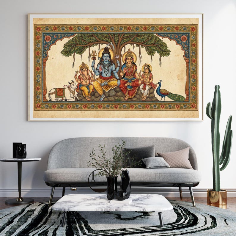 Puede incluir: Una obra de arte enmarcada y colorida que representa a una familia bajo un &aacute;rbol. Las figuras visten trajes tradicionales indios, con un pavo real y una vaca cerca. La obra tiene un marco dorado y cuelga sobre un sof&aacute; gris.
