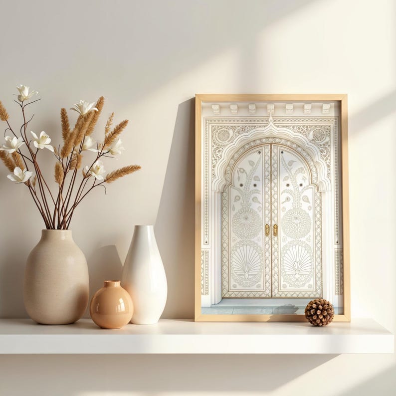 May include: A framed print of an ornate, arched doorway with intricate gold and white detailing. The print is displayed on a white shelf alongside a beige vase with dried flowers, a white vase, and a small orange vase. A decorative sphere is also on the shelf.
