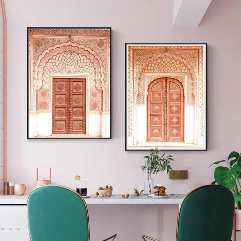 May include: Two framed prints of ornate archways and doors in shades of peach, coral, and cream. The doors feature detailed carvings and are set within elaborate archways. The prints are displayed above a white countertop with teal chairs.