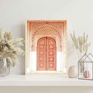 May include: A framed print featuring a detailed architectural design. The print showcases a coral-colored arched doorway with intricate carvings and a matching door. The frame is a light beige color, and the overall aesthetic is ornate and decorative.