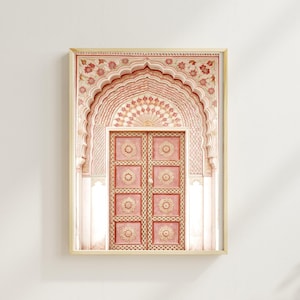 May include: Framed print of an ornate, pink door and archway. The door has eight panels with circular designs. The archway is intricately decorated with floral patterns in shades of pink and cream. The artwork is set in a light-colored wooden frame.
