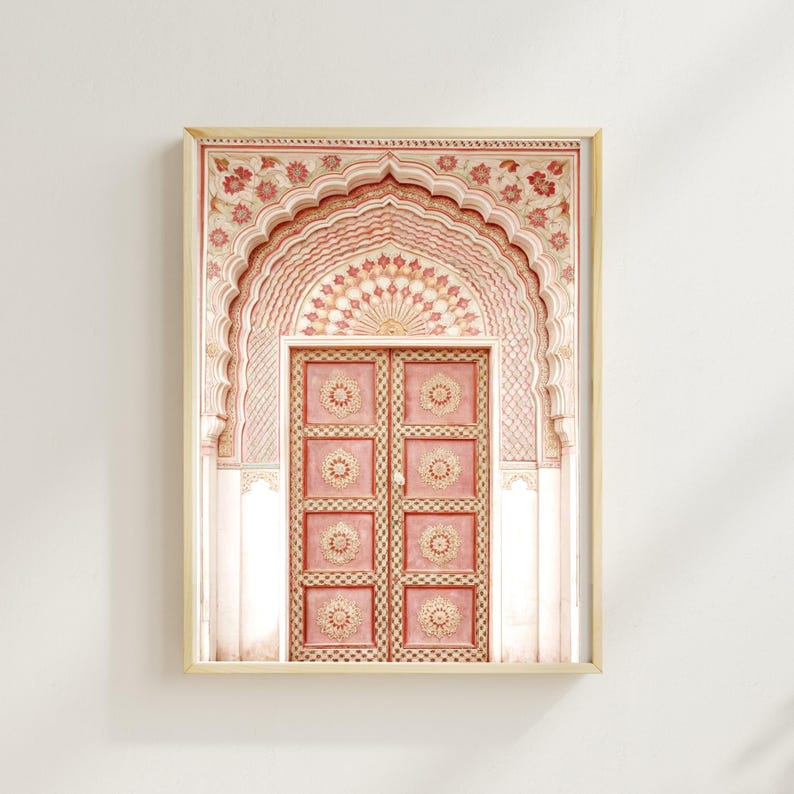 May include: Framed print of an ornate, pink door and archway. The door has eight panels with circular designs. The archway is intricately decorated with floral patterns in shades of pink and cream. The artwork is set in a light-colored wooden frame.