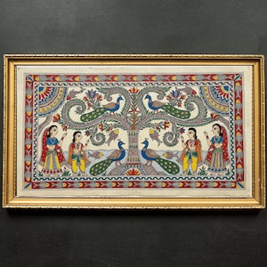 May include: A framed painting with a gold border, showcasing a tree with peacocks and figures in traditional Indian dress. The artwork uses a vibrant colour scheme of blues, greens, reds, and yellows. The painting is a detailed piece of art.
