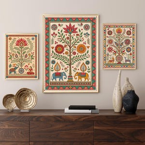 May include: Three framed art prints with gold frames, featuring colorful Indian folk art. The artwork depicts stylized trees, elephants, and floral patterns in red, blue, yellow, and green against a cream background. The prints are displayed above a dark wood cabinet.