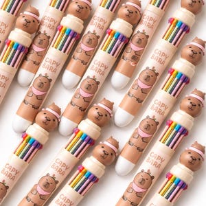 May include: A collection of Capybara-themed multi-color pens. Each pen features a brown capybara figure on top and a rainbow of colored pen tips. The pen barrels are light brown with the text "CAPY BARA" and a capybara illustration.