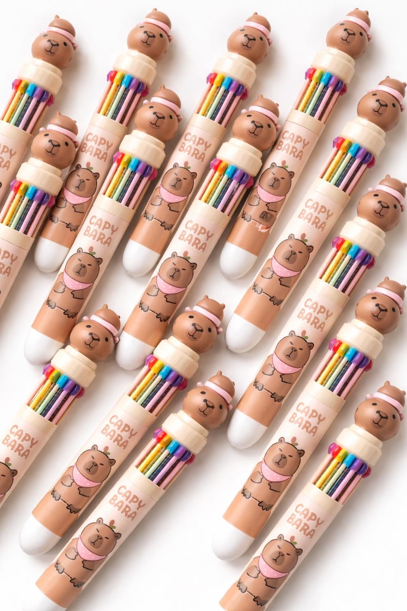 May include: A collection of Capybara-themed multi-color pens. Each pen features a brown capybara figure on top and a rainbow of colored pen tips. The pen barrels are light brown with the text "CAPY BARA" and a capybara illustration.