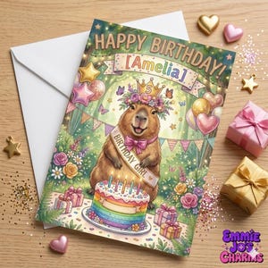 May include: A birthday card with a capybara illustration. The card reads "Happy Birthday! [Amelia]" and features a capybara wearing a crown and sash. A rainbow cake and gifts are also shown. The card is surrounded by decorative elements.