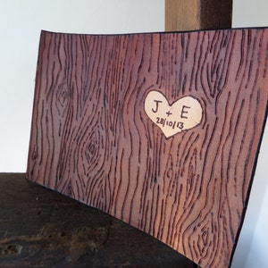 May include: A brown leather journal with a heart-shaped design carved into the front. The heart contains the initials "J + E" and the date "28/10/13".