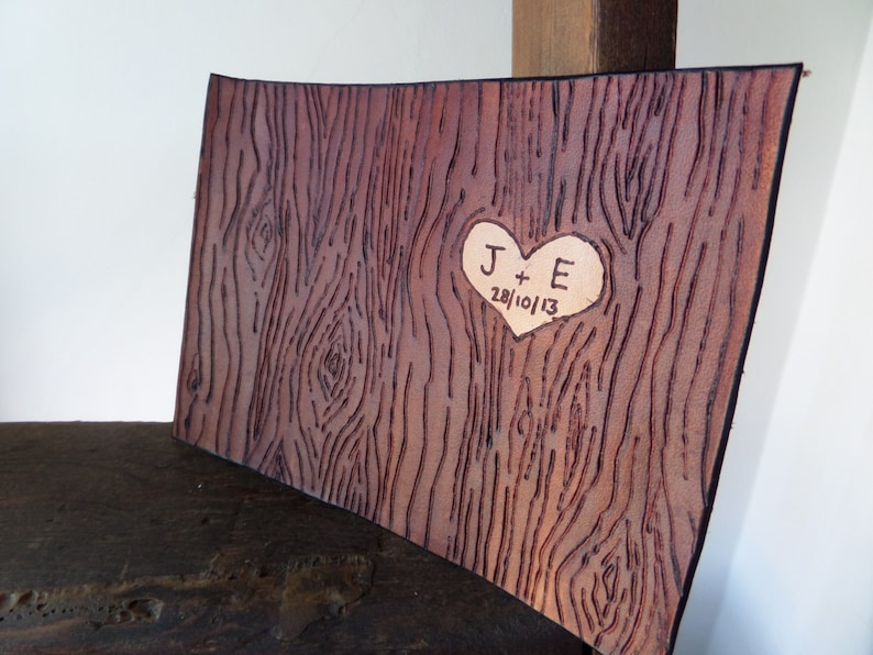 May include: A brown leather journal with a heart-shaped design carved into the front. The heart contains the initials "J + E" and the date "28/10/13".