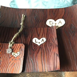 May include: Three wooden plaques with a wood grain pattern and heart-shaped designs. The plaques are engraved with the initials "D+A", "L+A", and "H+T" along with the date "6.16.12".