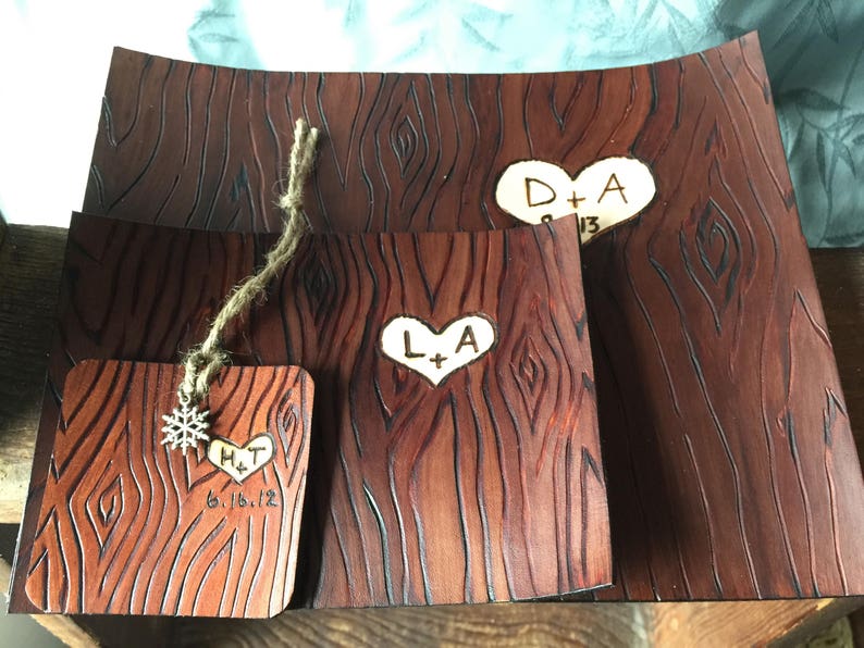 May include: Three wooden plaques with a wood grain pattern and heart-shaped designs. The plaques are engraved with the initials "D+A", "L+A", and "H+T" along with the date "6.16.12".