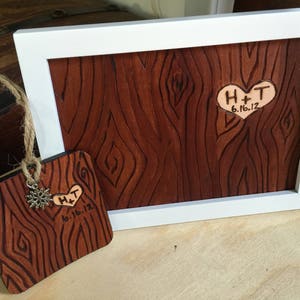 May include: A wooden plaque with a heart-shaped cutout and the initials "H+T" and the date "6.16.12" engraved. The plaque is framed in white and has a wood grain pattern.