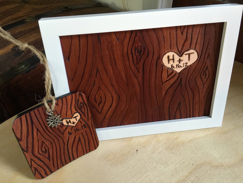 May include: A wooden plaque with a heart-shaped cutout and the initials "H+T" and the date "6.16.12" engraved. The plaque is framed in white and has a wood grain pattern.