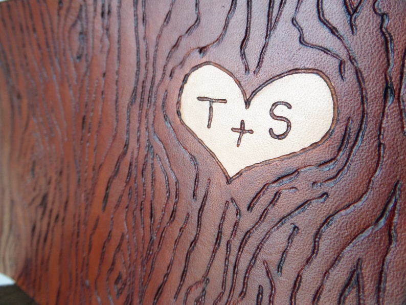 May include: A brown leather surface with a carved heart shape. The heart is filled with a lighter brown leather and has the initials "T + S" carved into it.