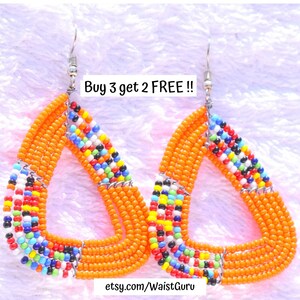 May include: A pair of orange beaded earrings in a triangular shape. The earrings have a silver hook and are adorned with colorful beads in a geometric pattern. The text "Buy 3 get 2 FREE !!" is visible.