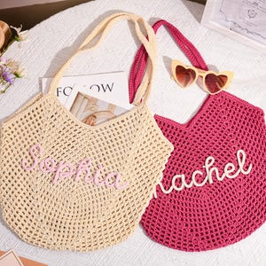 May include: Two crochet tote bags. One is beige with the name "Sophia" in pink script. The other is magenta with the name "Rachel" in white script. Both have matching handles. Heart-shaped sunglasses rest on the magenta bag.