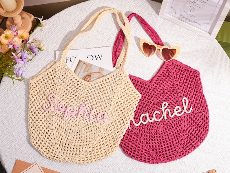 May include: Two crochet tote bags. One is beige with the name "Sophia" in pink script. The other is magenta with the name "Rachel" in white script. Both have matching handles. Heart-shaped sunglasses rest on the magenta bag.