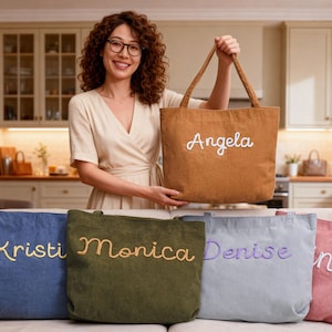 Puede incluir: Una mujer sostiene un bolso tote marrón bordado con el nombre "Angela" en escritura blanca. Se ven cuatro bolsos tote adicionales en azul, verde, gris y rosa, cada uno con un nombre bordado diferente.