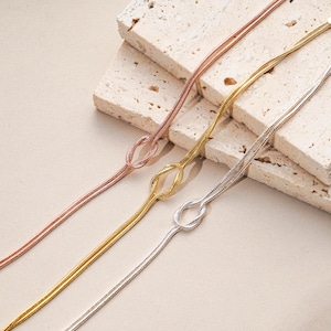 K&ouml;nnte beinhalten: Drei zarte Halsketten in Ros&eacute;gold, Gold und Silber, jede mit einem Knotendesign. Die Halsketten werden auf einer neutralen Oberfl&auml;che pr&auml;sentiert, die ihren schlanken und minimalistischen Stil hervorhebt. Der Schmuck ist ein perfektes Accessoire f&uuml;r jedes Outfit.